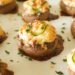 Stuffed mushroom poppers on parchment paper with browned cheese and sliced jalepeno and parsley garnish.